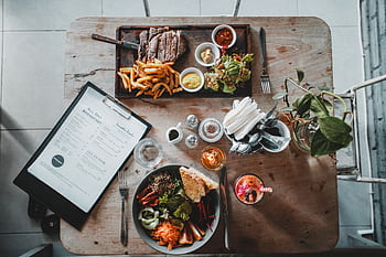 Top-down view of a well-arranged meal including steak, salad, and beverage in a cozy café setting. HD wallpaper