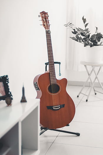 A classic acoustic guitar stands elegantly in a bright, minimalist indoor setting, surrounded by modern decor. HD phone wallpaper
