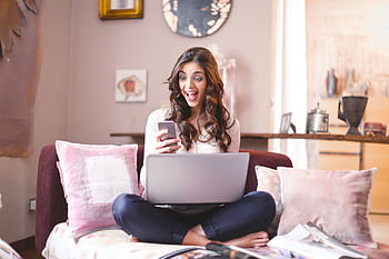 Smiling woman at home, using smart and laptop, expressing surprise and happiness. HD wallpaper