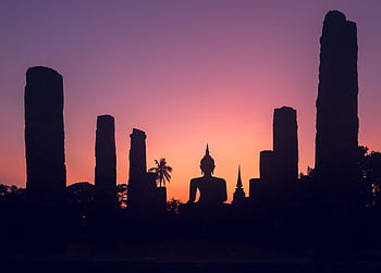 Tranquil silhouette of a Buddha statue at sunset in Sukhothai Historical Park, Thailand. HD wallpaper