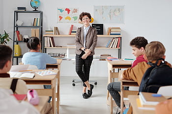 Teacher engaging with diverse students in a modern classroom setting for education. HD wallpaper
