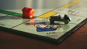 Close-up shot of a Monopoly board game featuring a toy car and a red house on 'Go to Jail'. HD wallpaper