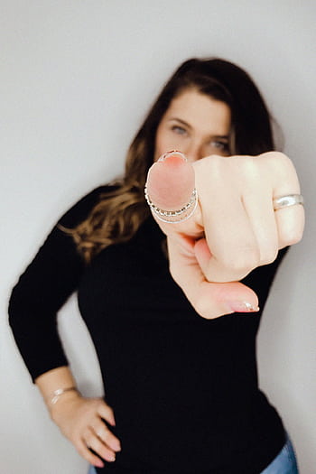A confident woman points forward in a stylish and assertive pose, showcasing fashionable rings and attire. HD phone wallpaper