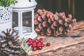 A cozy rustic scene with a candle lantern, pinecones, and cranberries on a wooden table, perfect for winter decor. HD wallpaper