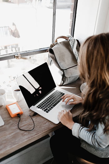 A young woman works remotely at a café, using her laptop and external hard drive. HD phone wallpaper