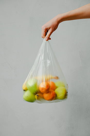 A hand holding a transparent plastic bag full of fresh citrus fruits against a neutral background. HD phone wallpaper
