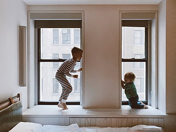 Two children playing on a window seat in a cozy indoor setting, showcasing joy and family bonds. HD wallpaper