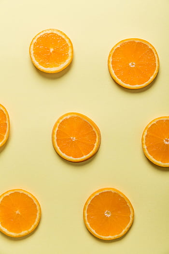 Vibrant sliced oranges arranged on a pastel yellow background, evoking freshness. HD phone wallpaper