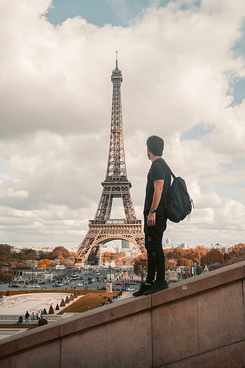 A tourist stands with a backpack admiring the Eiffel Tower in Paris during the day. HD phone wallpaper