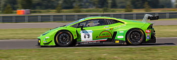 High-speed green sports car racing on circuit track during daytime. HD wallpaper