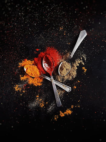A creative flat lay of colorful spices - red, orange, and brown - with metal spoons on a dark background. HD phone wallpaper