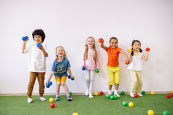 Happy diverse children playing with colorful balls indoors, showcasing fun and friendship. HD wallpaper