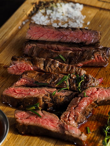 Close-up of sliced grilled steak with seasoning on a wooden board, highlighting texture and juiciness. HD phone wallpaper