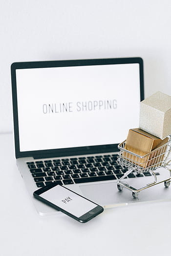 Minimalist setup showcasing online shopping with a laptop and miniature cart. HD phone wallpaper