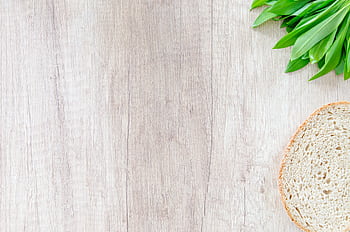Slice of bread and green leaves on a wooden surface. Perfect for food and health-related content. HD wallpaper