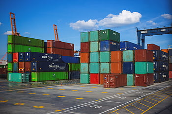 Vibrant shipping containers stacked at an industrial port under a blue sky. HD wallpaper