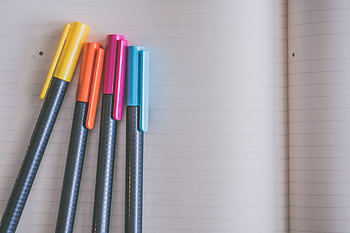 A collection of colorful pens resting on an open lined notebook, creating a vibrant and inviting workspace. HD wallpaper