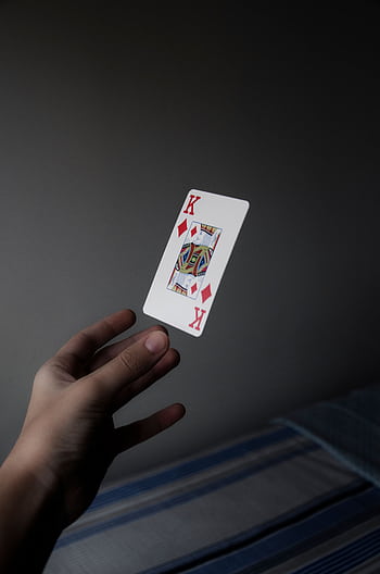 A hand elegantly holds a floating King of Diamonds card against a subdued background. HD phone wallpaper