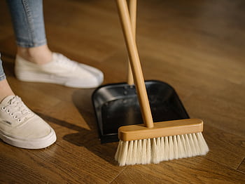 Close-up of cleaning process with broom and dustpan beside sneakers on a wooden indoor floor. HD wallpaper