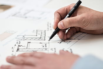 Close-up of hand drawing intricate technical designs on blueprint with pen, ideal for engineering or architecture themes. HD wallpaper