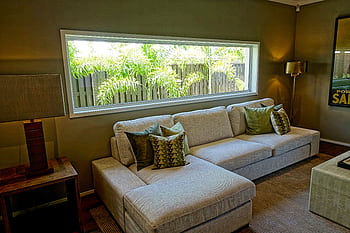 Cozy modern living room featuring a large sofa, decorative pillows, and a wide window with outdoor views. HD wallpaper