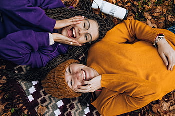 Two friends smiling, enjoying fall colors while lying on autumn leaves outdoors. HD wallpaper