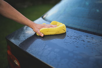 Hand cleaning car with a yellow sponge, showcasing car detailing and washing process. HD wallpaper