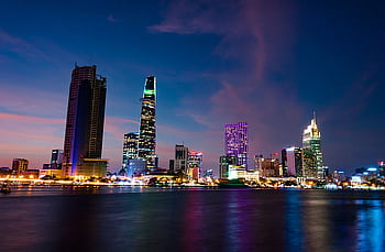 A stunning evening view of Ho Chi Minh City's skyline reflecting vibrant lights over the Saigon River. HD wallpaper