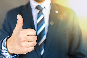 Close-up of a businessman in a suit giving a thumbs-up in a bright, positive setting. HD wallpaper