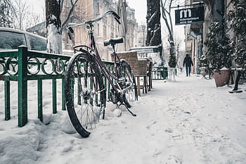 Snow-covered street in Bucharest featuring a bicycle with buildings in the background. HD wallpaper