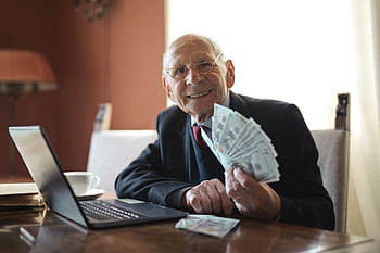 Happy senior businessman showing cash at his desk with a laptop, indoors. HD wallpaper