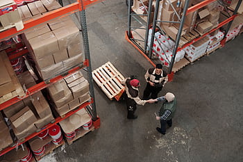 High angle view of workers shaking hands in a warehouse, symbolizing teamwork and logistics. HD wallpaper