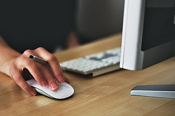 A hand using a wireless mouse at a modern desk setup with a computer and keyboard. HD wallpaper