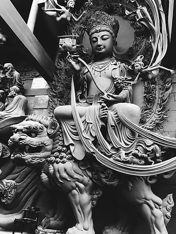 A detailed black and white sculpture of a Buddhist deity in a serene temple setting. HD phone wallpaper