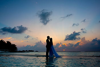 A couple shares a romantic moment on a tropical beach during a beautiful sunset, symbolizing love and serenity. HD wallpaper
