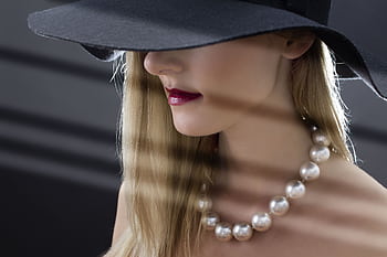 Close-up portrait of a stylish woman wearing a hat and pearl necklace with soft lighting and shadows. HD wallpaper