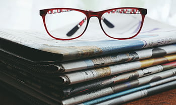 Red eyeglasses resting on a stack of newspapers symbolize reading and information. HD wallpaper