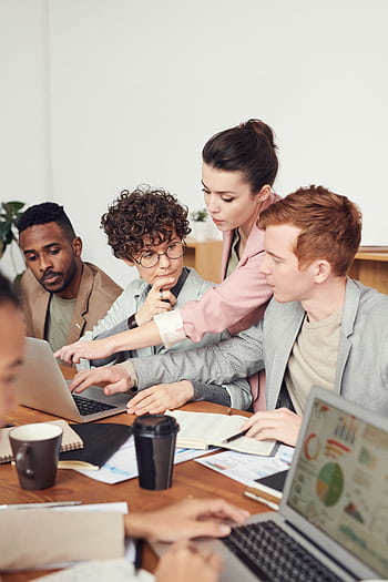A group of professionals engaged in a collaborative office meeting, discussing ideas with laptops. HD phone wallpaper