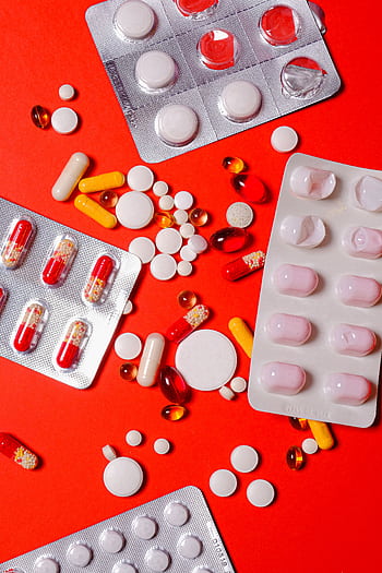 A close-up of various pills and capsules on a vibrant red background, highlighting healthcare and medicine. HD phone wallpaper