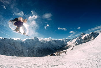 Snowboarder performing a high jump in a que snow-covered mountain landscape during the day. HD wallpaper