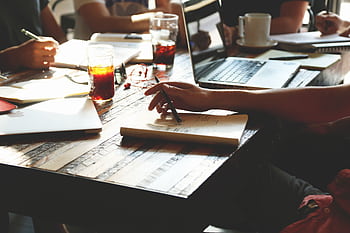 A group of adults engaged in a collaborative office meeting, discussing ideas with notes, laptops, and refreshments. HD wallpaper