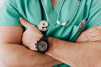 Close-up of a healthcare professional with arms crossed wearing medical scrubs and stethoscope. HD wallpaper