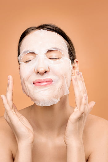 Woman smiling with a sheet face mask, embracing a skincare self-care moment. HD phone wallpaper