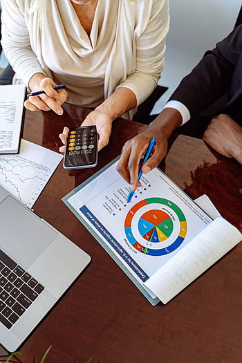 Two business professionals discussing financial documents and strategies at an office desk. HD phone wallpaper