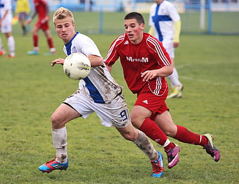 Two teenage soccer players competing fiercely on a muddy grass field. HD wallpaper