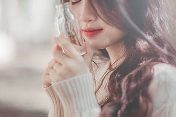 Close-up of a serene woman with long hair holding a glass bottle. Soft and warm tones. HD wallpaper