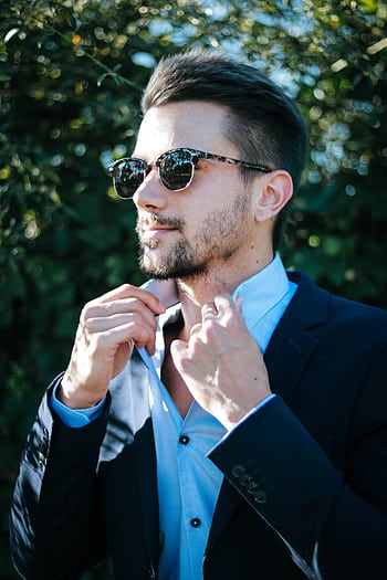 Fashionable man adjusting his suit and sunglasses outdoors on a sunny day. HD phone wallpaper