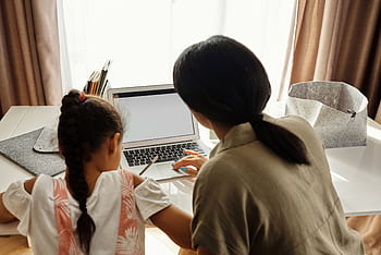 A mother helps her daughter with online learning on a laptop at home, emphasizing family education. HD wallpaper