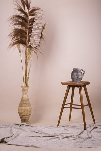 A minimalist composition featuring a vase of dried flowers and a jug on a stool against a beige backdrop. HD phone wallpaper