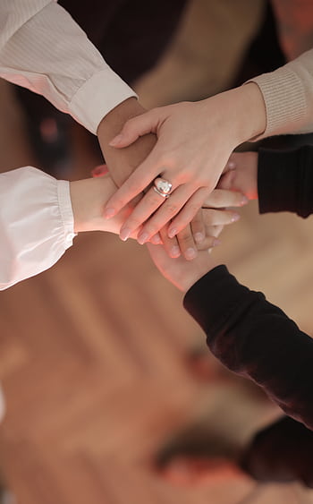 Overhead view of diverse hands stacked in unity, symbolizing teamwork and cooperation. HD phone wallpaper